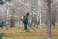 Migrant worker sweeping leaves in the park with a knapsack blower.